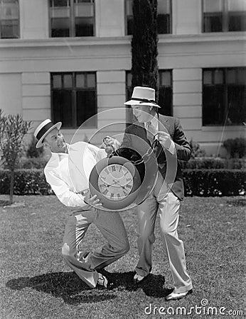 Two men wrestling with an oversized pocket watch Stock Photo