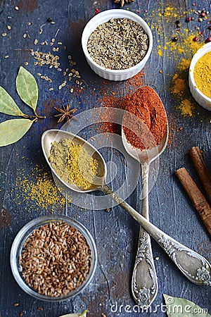 Two metal spoons with spices, bay leaf, flax seeds, dill, cinnamon sticks on a dark rustic background. View from above Stock Photo