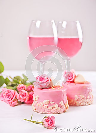 Two mini cakes, glasses with pink grape wine and rose flowers on a white table. Romantic dinner concept Stock Photo