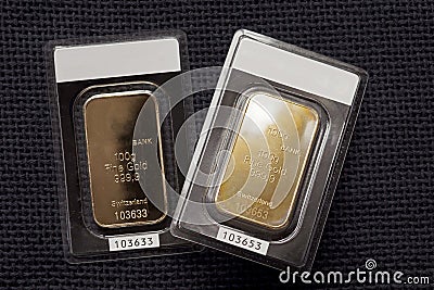 Two minted gold bars against a dark fabric texture Stock Photo