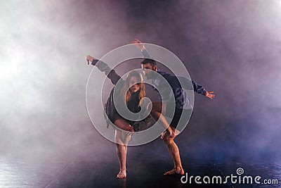 Two modern dancers stretching their shoe-less feet high in the air surrounded by smoke on stage Stock Photo