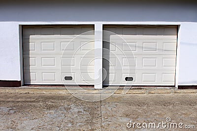 Two modern white rollup garage doors with cracked concrete driveway mounted on white wall Stock Photo
