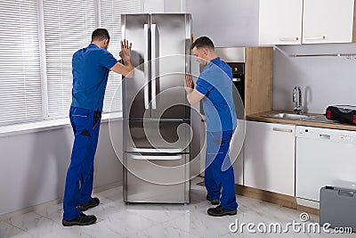 Two Movers Placing Refrigerator In Kitchen Stock Photo