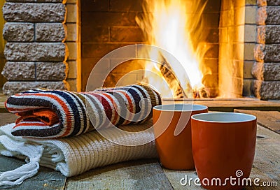 Two mugs for tea or coffee, woolen things near cozy fireplace. Stock Photo