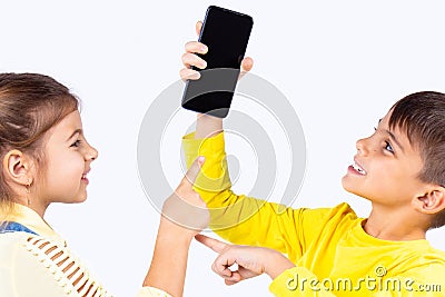 Two nice kids boy and girl fighting for the smart phone, the boy holding the phone in his hand and the girl wants to Stock Photo