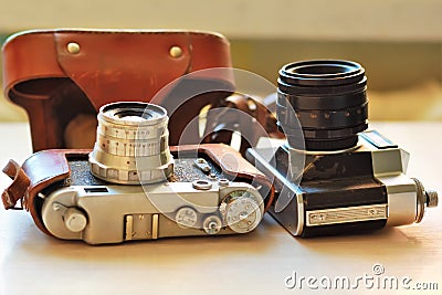 Two old school vintage photo cameras on light brown table. One in brown retro leather case holder Stock Photo