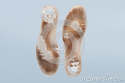 Two old, shabby orthopedic insoles isolated on blue background. Dirty leather insoles. Worn out things with holes. Inner Stock Photo