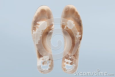 Two old, shabby orthopedic insoles isolated on blue background. Dirty leather insoles. Worn out things with holes. Inner Stock Photo