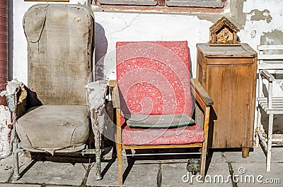 Two old vintage retro broken reclining seats porvanoy cloth on a background of white whitewashed wall with cracks and old bedside Stock Photo