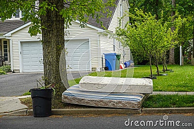 Two old worn out mattresses by a tree at the curb near a trash can in front of a house Stock Photo