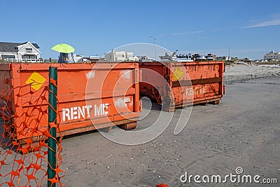 Two orange dumpsters at construction site on a wet sandy beach that say rent me on them Stock Photo
