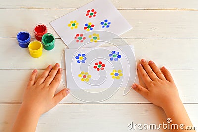 Two paintings of flowers painted children fingers. Jars with gouache. Children hands are on the table Stock Photo