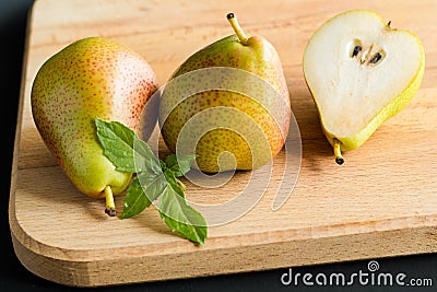 Two pears and piece of a pear with fresh basil leaves on a wooden cutting board, side view Stock Photo