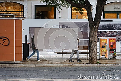Two people carrying a large white board on the sidewalk in Lisbon, Portugal Editorial Stock Photo