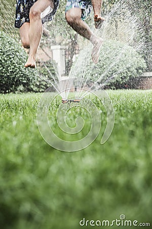 Two people jumping through a sprinkler, mid-air, surface level shot Stock Photo