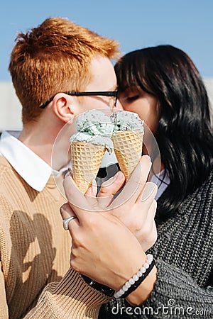 Two people in love sitting outdoors, holding ice cream, sensually kissing Stock Photo