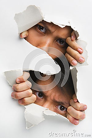 Two people peeking from hole in wall Stock Photo