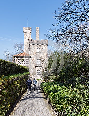 Two people walk along the path along the green alley on the background of an ancient castle Editorial Stock Photo