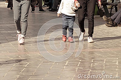 Two people wearing jeans and child girl wearing woolen clothing walking through the pedestrian walkway in summer vacation Stock Photo