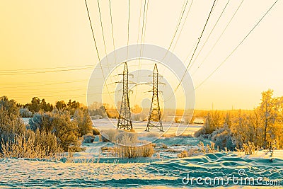 Two pillars of high voltage line and wires through riverplain in winter. Sunset Stock Photo