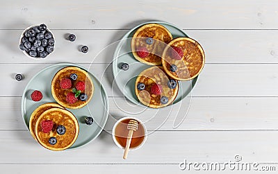 Two plates with tasty american pancakes with raspberries, blueberries, and honey. Top view, wooden table. Stock Photo