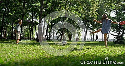 Two playful siblings kick football ball in city garden. Kids rest on sunny day Stock Photo