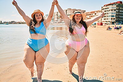 Two plus size overweight sisters twins women happy and proud of their bodies walking at the beach on summer holidays Stock Photo