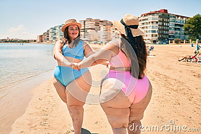 Two plus size overweight sisters twins women happy and proud of their bodies walking at the beach on summer holidays Stock Photo