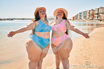 Two plus size overweight sisters twins women happy and proud of their bodies walking at the beach on summer holidays Stock Photo