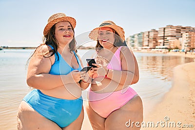 Two plus size overweight sisters twins women happy with smartphone at the beach on summer holidays Stock Photo