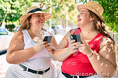 Two plus size overweight sisters twins women with smartphone outdoors on a sunny day Stock Photo