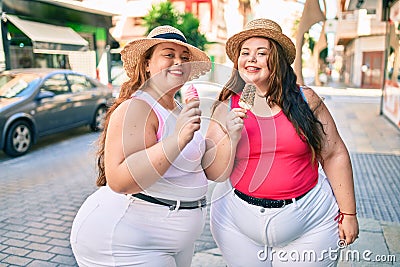 Two plus size overweight sisters twins women smiling eating an ice cream outdoors Stock Photo