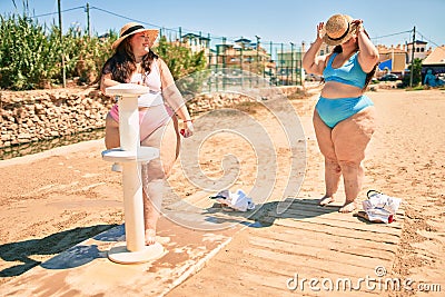 Two plus size overweight sisters twins women washing sand on foot shower at the beach Stock Photo
