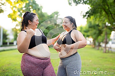 Two plus size woman share a moment during their workout in green park, embodying joy and fitness. Stock Photo