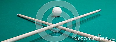 two pool cues crossed in front of a white ball on a green table Stock Photo