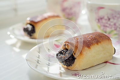 Two poppy buns in white romantic saucers on a white table. Tea time. Side view Stock Photo