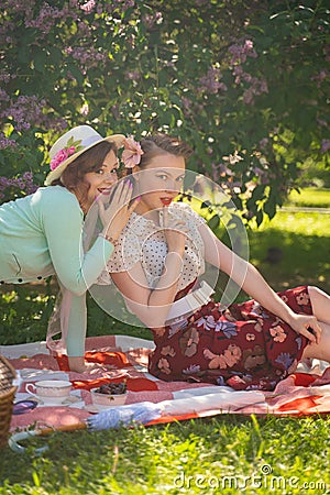 Two pretty girls friends sitting on the red blanket on the green grass and have summer picnic. happy woman having rest and fun on Stock Photo