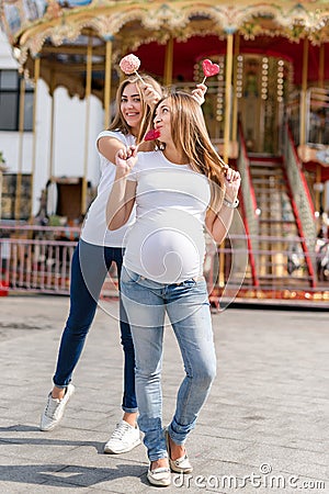Two pretty women in amusement park having fun and eating sweets, happy family. Samesex lesbian family, pregnant couple. Stock Photo