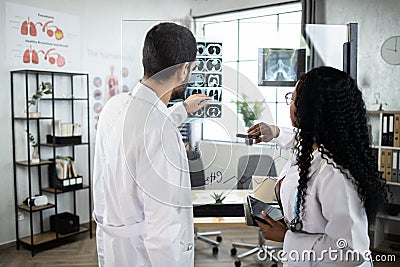 Two qualified multiethnic doctors, standing near the office glass board and interpreting CT scan Stock Photo
