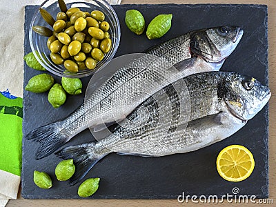 Two ready to cook raw fish with lemon and olives on stone slate Stock Photo