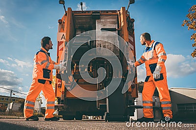 Two refuse collection workers loading garbage into waste truck Stock Photo