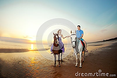 Two riders on horseback at sunset on the beach. Lovers ride horseback. Young beautiful man and woman with a horses at the sea. Stock Photo