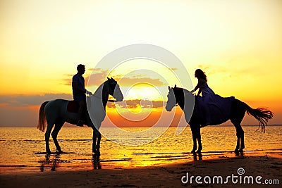 Two riders on horseback at sunset on the beach. Lovers ride horseback. Young beautiful man and woman with a horse at the sea. Rom Stock Photo