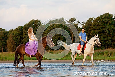 Two riders on horseback at sunset on the beach. Lovers ride horseback. Young beautiful man and woman with a horses at the sea. Stock Photo