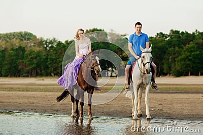 Two riders on horseback at sunset on the beach. Lovers ride horseback. Young beautiful man and woman with a horses at the sea. Stock Photo