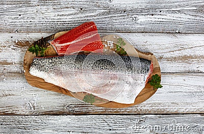 Two Salmon trout fillet, skin side up and down, on natural olive wood server with parsley and salt seasonings Stock Photo