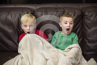 Two scared little boys sitting on a couch watching TV Stock Photo