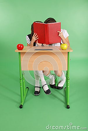 Two school girl sharing secrets sitting at a desk from book Stock Photo