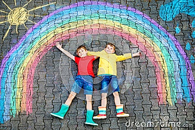 Two school kids boys having fun with with rainbow picture drawing with colorful chalks on asphalt. Siblings, twins and Stock Photo