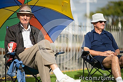 Two senior men , one under colourful sun umbrella sitting on grass during 60th National Jazz Festival in city Editorial Stock Photo